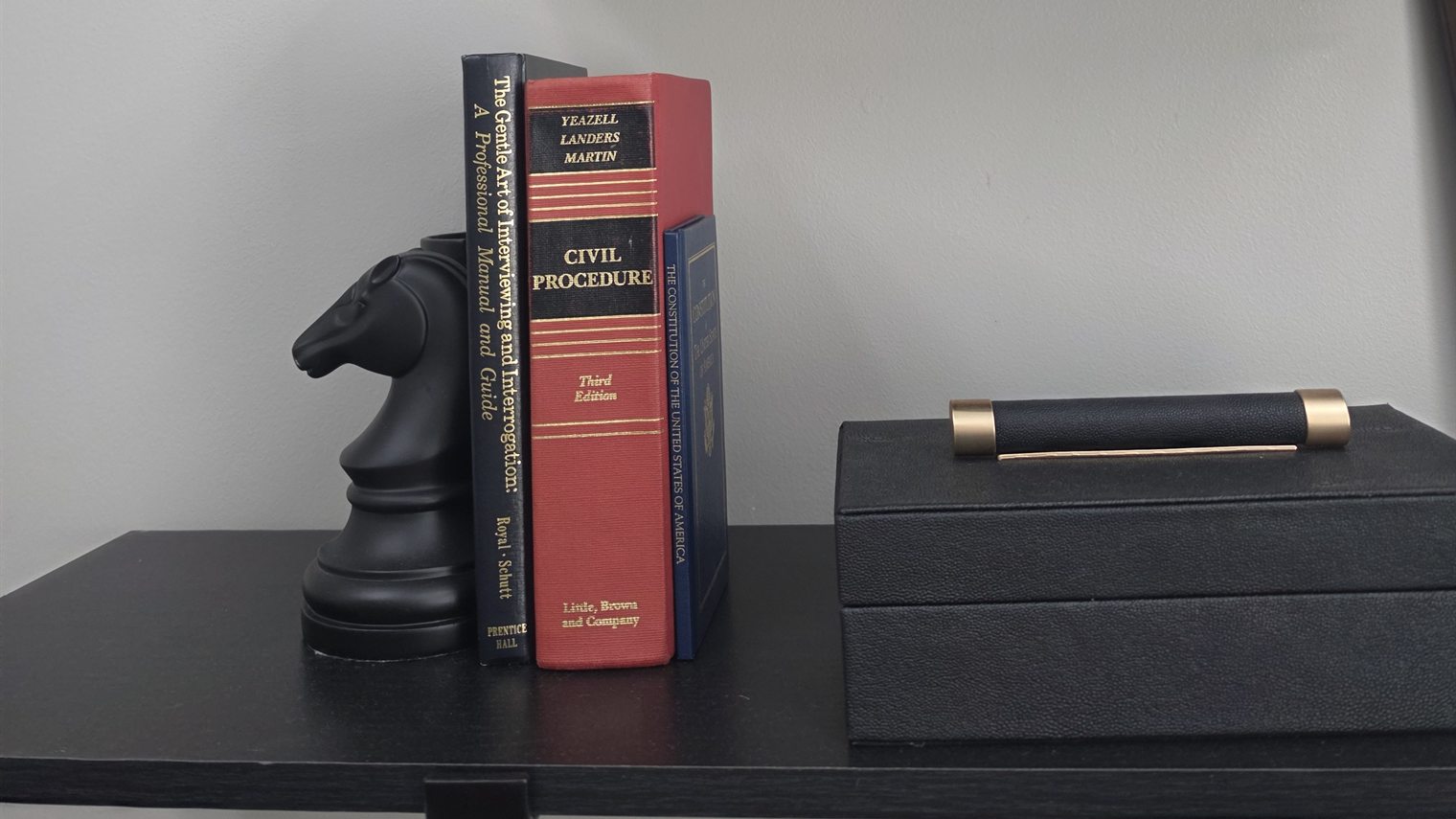 A black knight bookend holding a civil procedure casebook, a pocket Constitution, and a manual on interviewing, on a shelf in a Panama City Beach law office