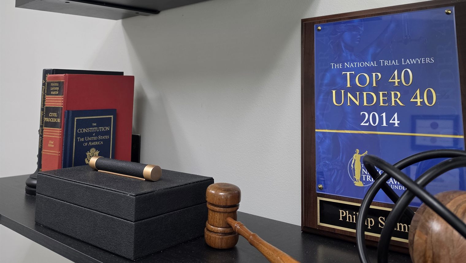 Law books, a gavel, and a National Trial Lawyers Top 40 Under 40 plaque on a shelf in Phillip Stamman's Panama City Beach law office