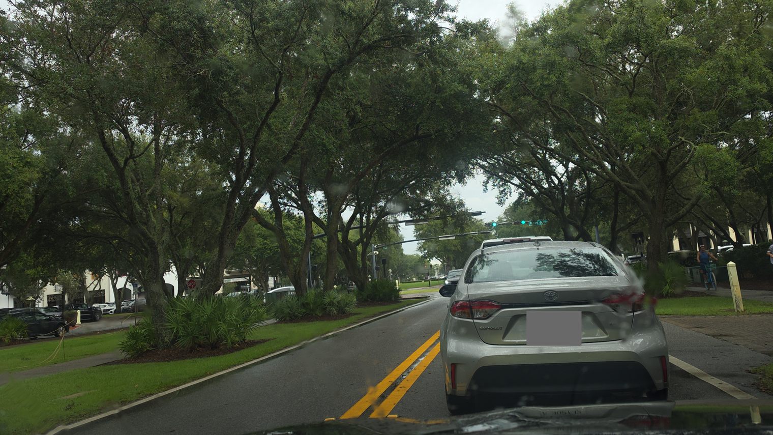 View through a rain-spotted windshield of a car stopped in traffic on a tree-lined street in Rosemary Beach along 30A in Walton County, Florida